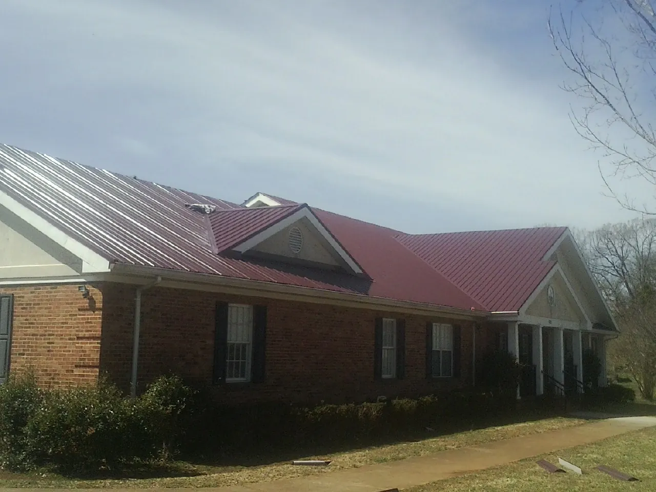 Red metal roof with gabled entries on a long brick building, from a Hail Damage Roof Repair job in Lake Station