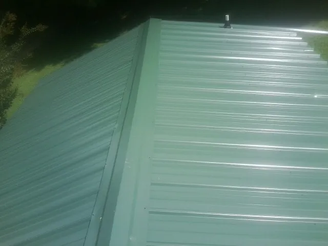 New green metal panels meeting at the ridge of a roof — Flat Roof Repair work by our crew in Lake Station