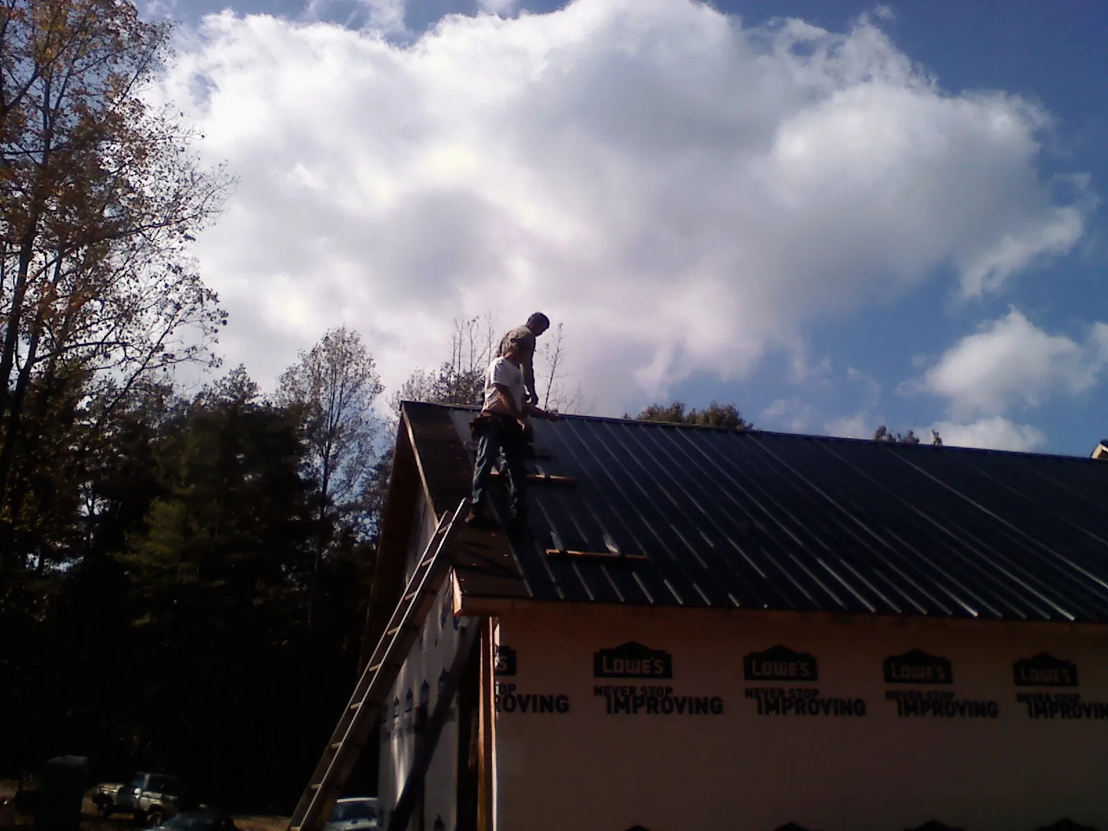 Roofer fastening dark metal panels high against a cloudy sky, from a Roof Inspection job in Lake Station