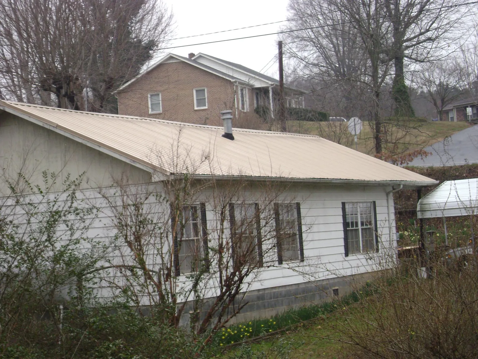 Tan metal roof on a white sided house set into a hillside — Commercial Roofing by Roofing Brothers in Lake Station