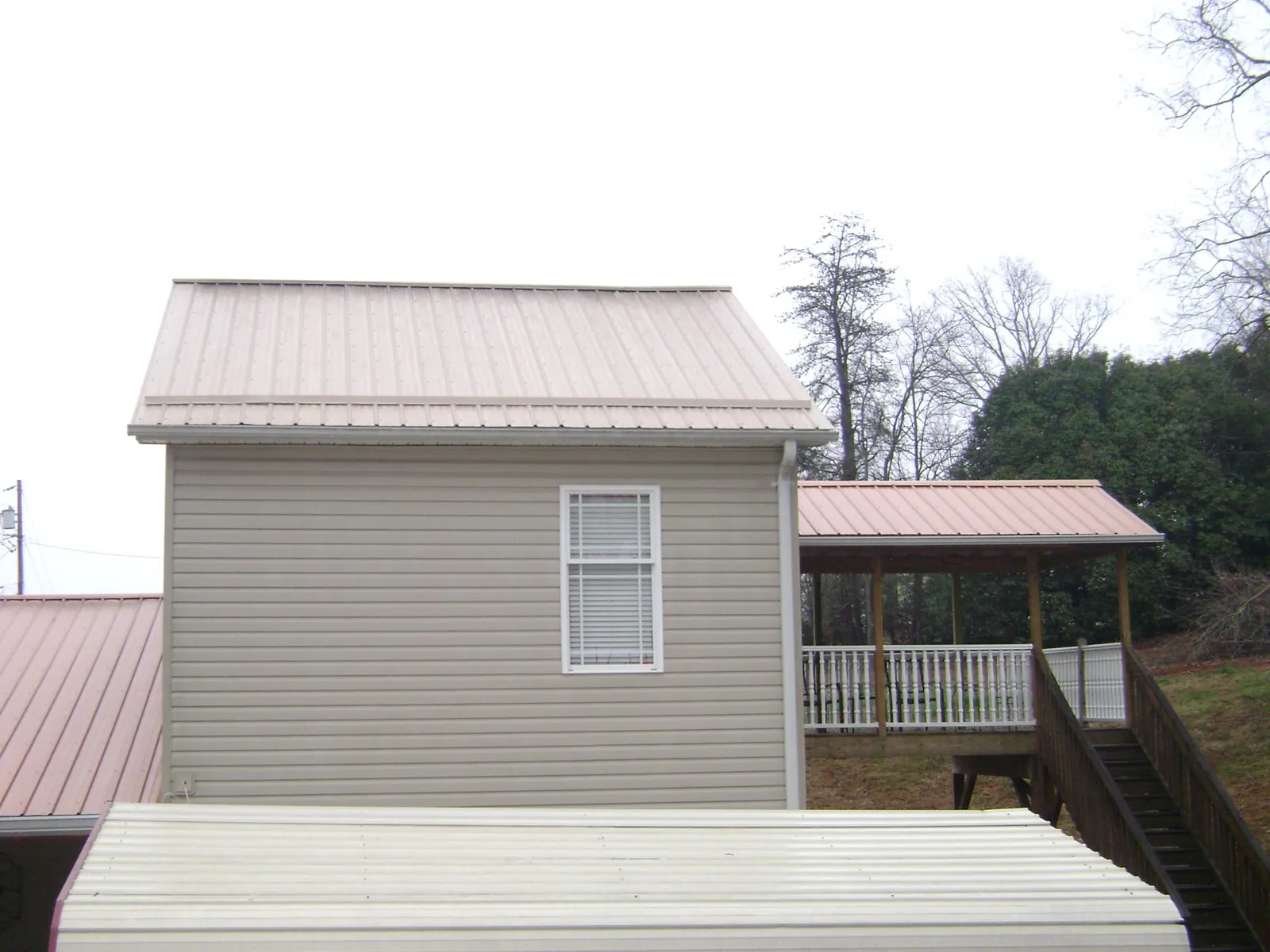 Tan metal roofs on a two story addition and attached porch, from a Roof Replacement job in Lake Station
